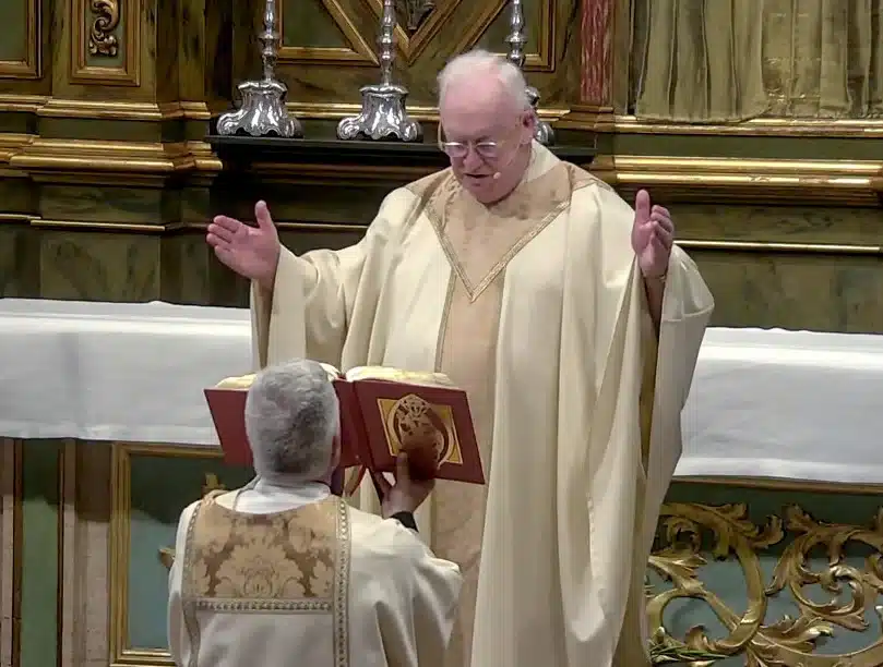 priest in white robe with hands raised and head down
